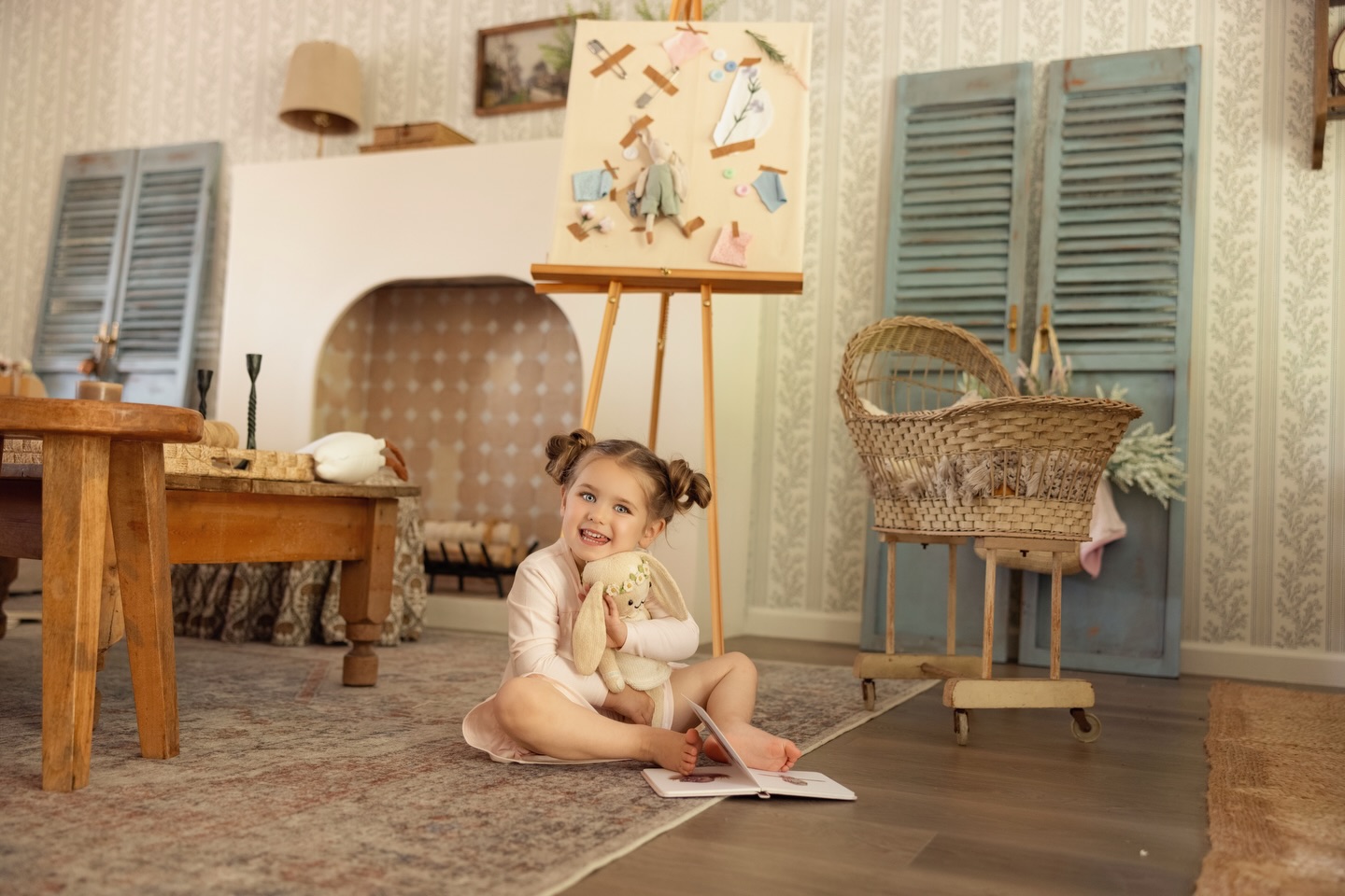 A girl with pigtails sitting cross-legged on a rug, hugging a plush bunny