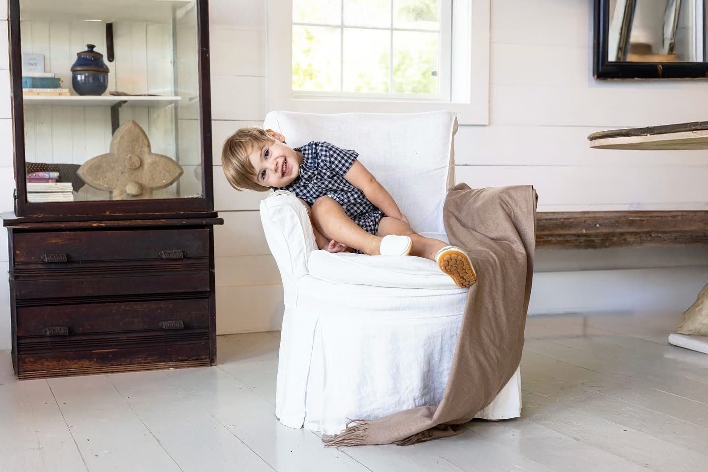 A laughing toddler draped over a white armchair