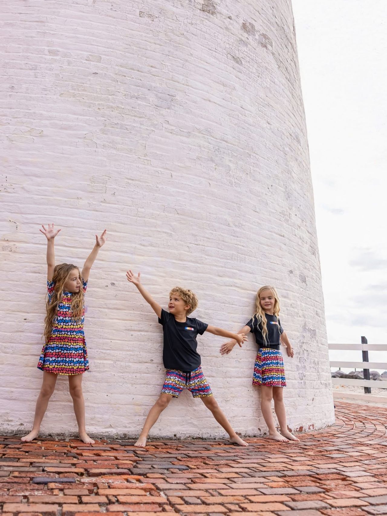 Three children striking poses against a white brick wall