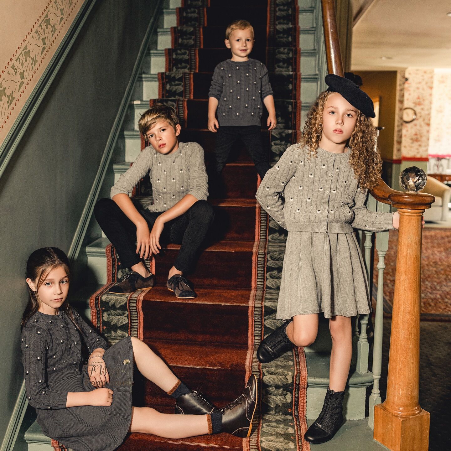 Four children in matching grey knits posing together on a carpeted staircase