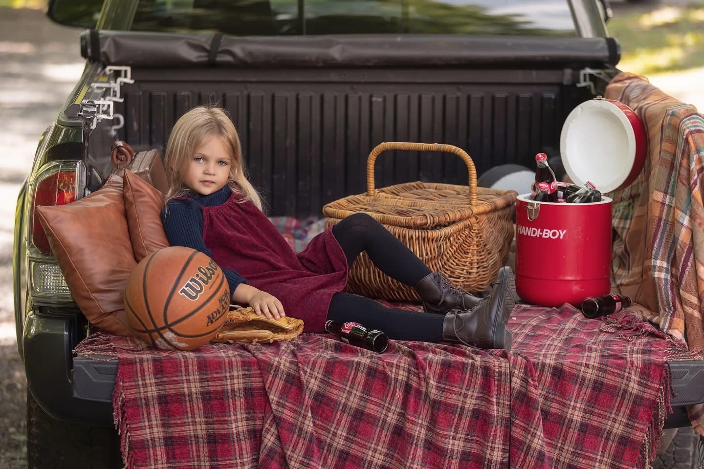 A girl in a pinafore dress lounging in the bed of a pickup truck with sports gear