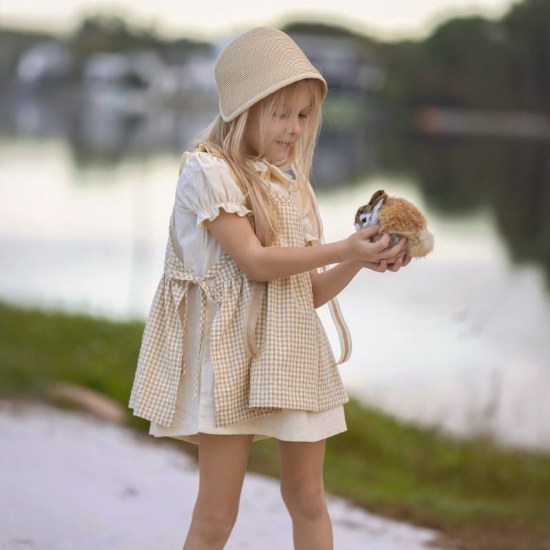 A little girl in a bonnet standing by the water, holding a plush bunny