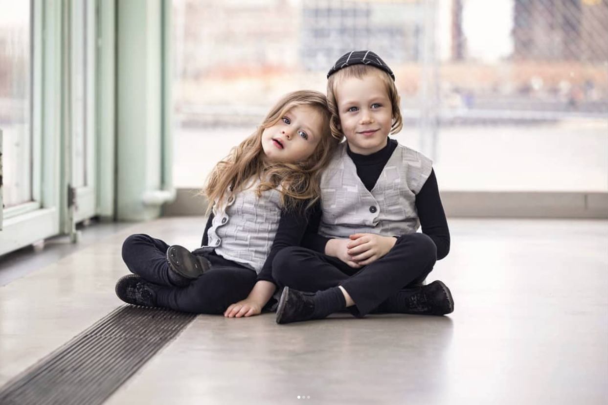 A girl resting her head on her brother's shoulder as they sit together on the floor