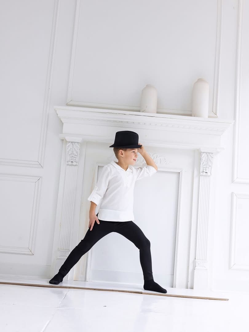 A boy posing with a black hat in a white paneled room