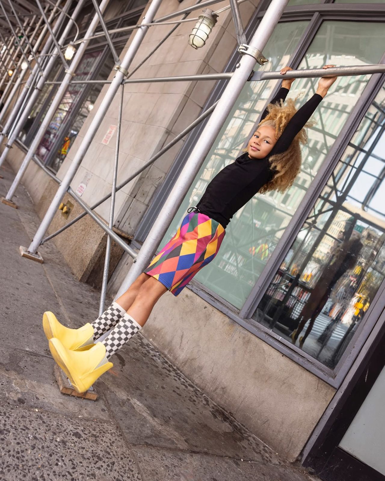 A boy hanging from a scaffolding pole on a city sidewalk