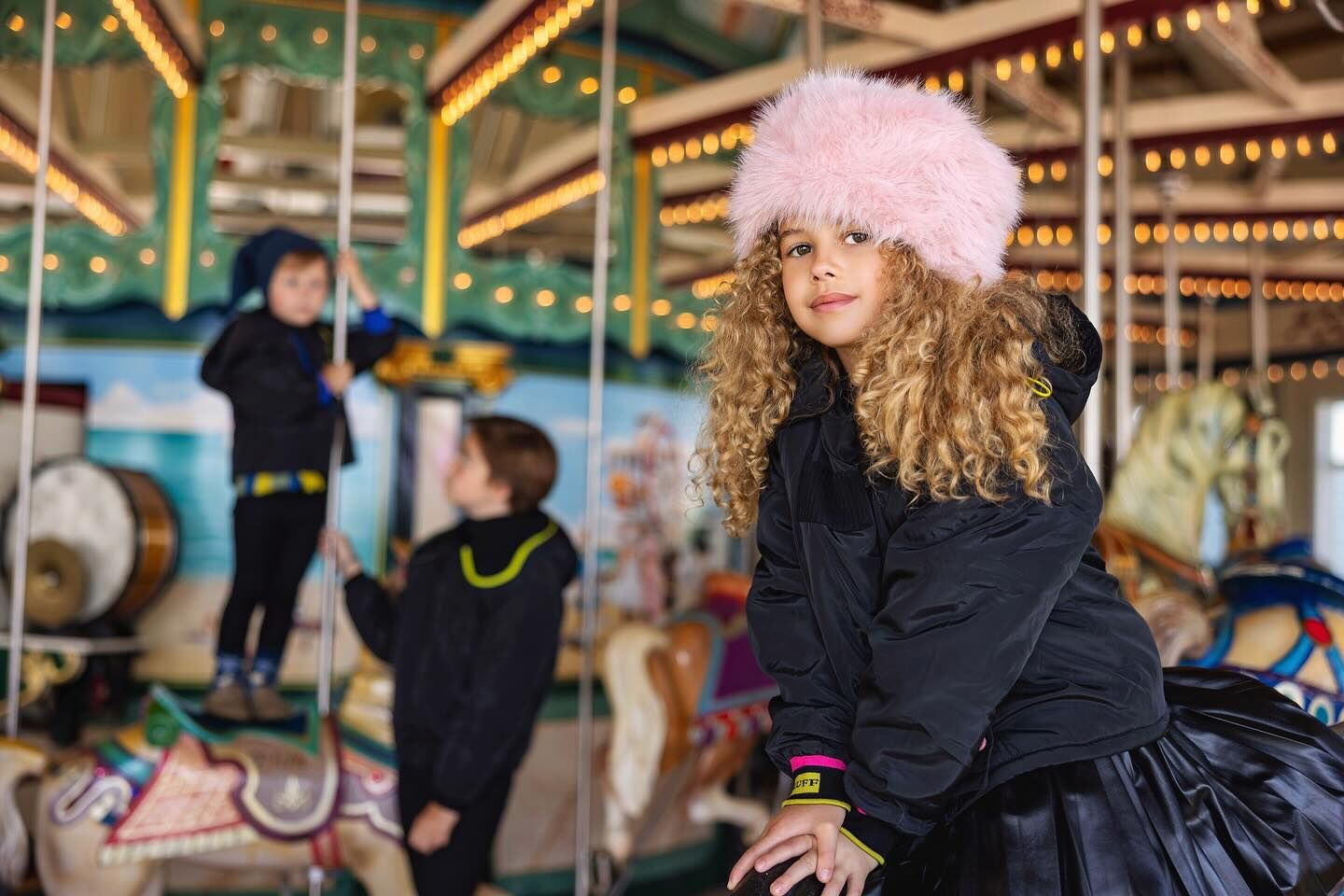 A girl in a pink fur hat beside a lit carousel